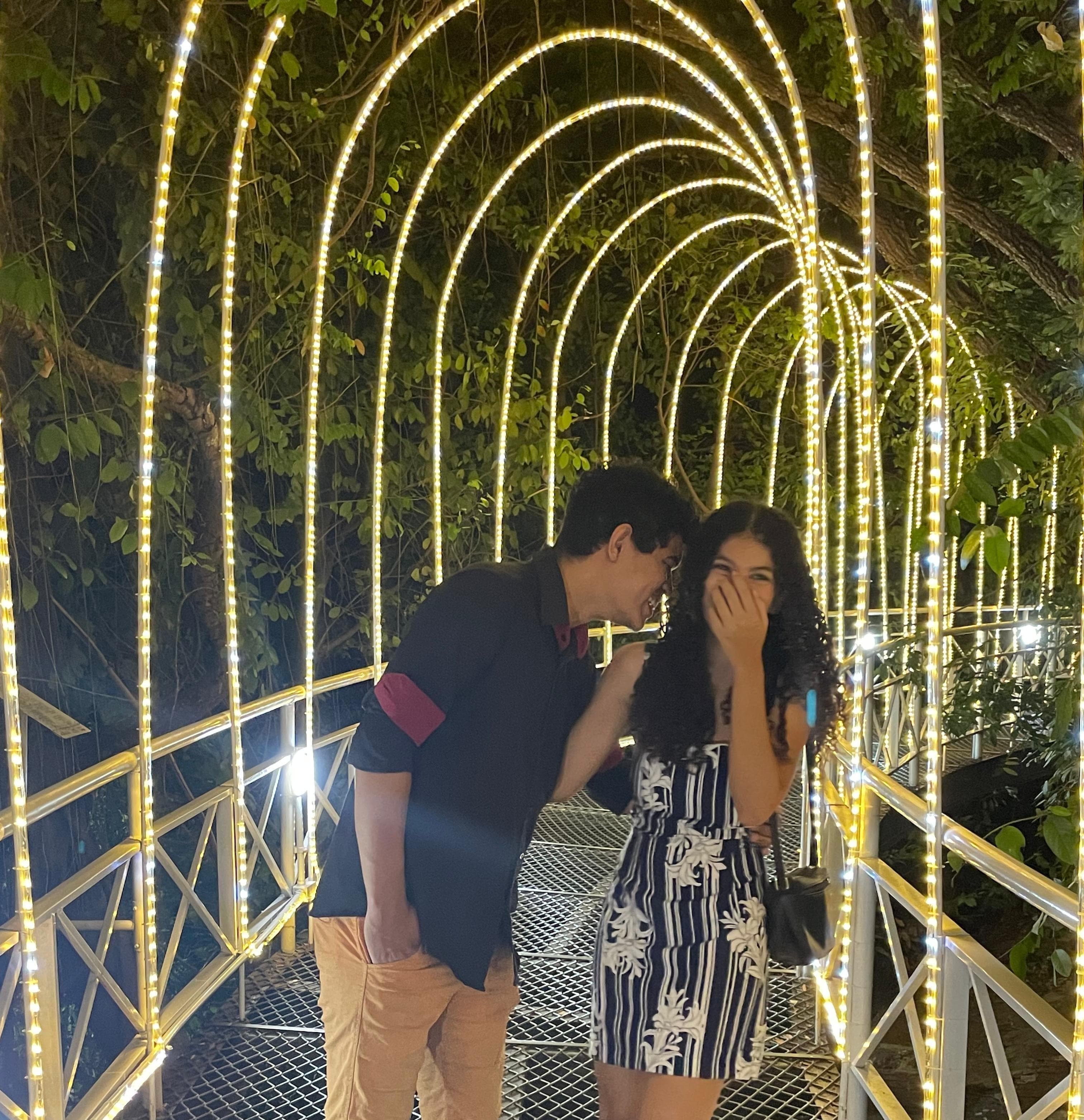 Caio e Carla rindo sob um túnel de luzes em 2023